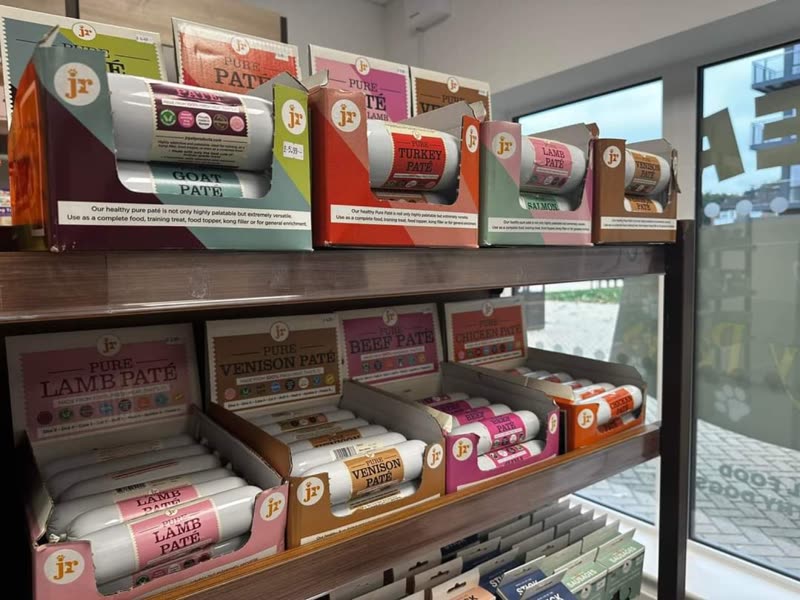 Shelving stacked with boxed and packaged raw dog food beside the shop window